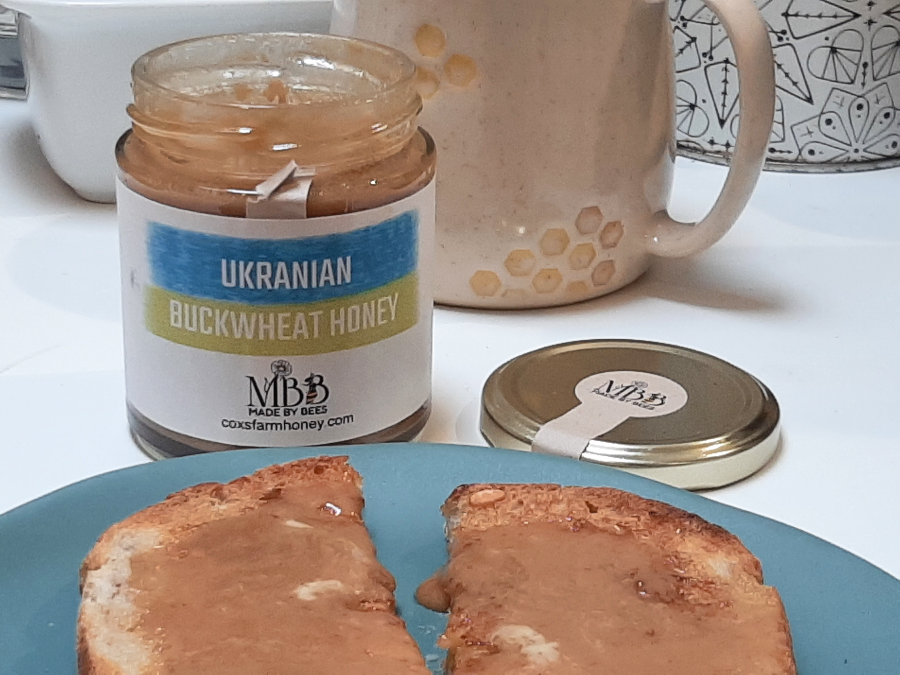 Jar of Ukrainian buckwheat honey on a plate with toast, next to a mug.